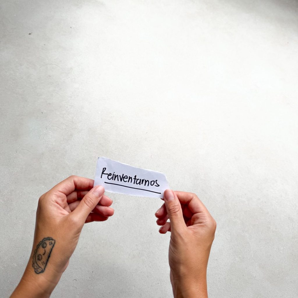 Manos sosteniendo un papel con la palabra Reinventarnos escrita a mano, categoría Historias que Inspiran